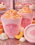 Two pink containers of 'Body Frosting' with peach slices and whipped cream on a pink background.