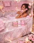 Woman in a bathtub with bae bakerie products and candles, surrounded by pink decor.