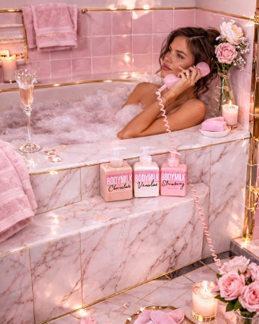 Woman in a bathtub with bae bakerie products and candles, surrounded by pink decor.